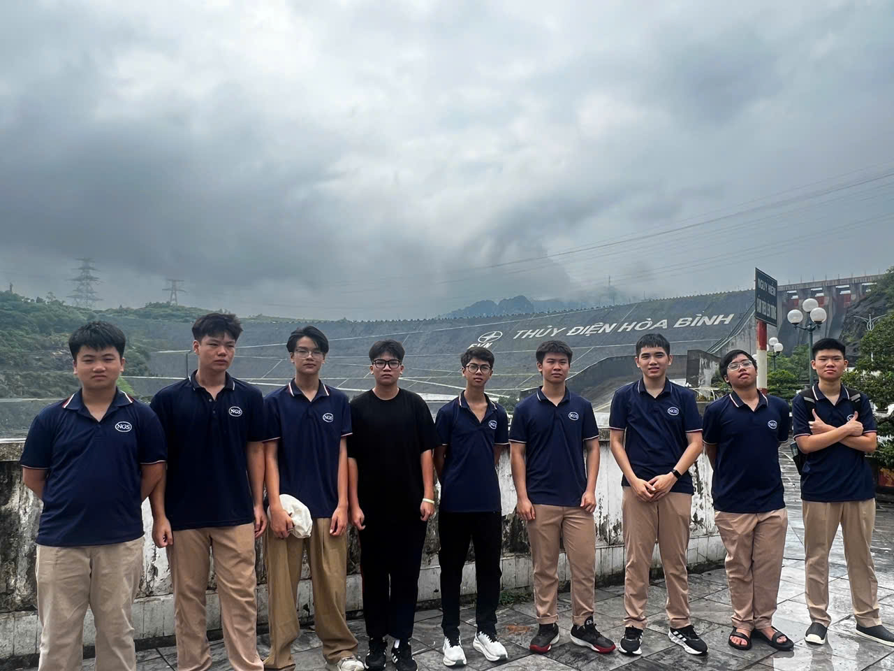 Nhóm học sinh nam chụp ảnh trước thân đập có dòng chữ Thuỷ điện Hoà Bình